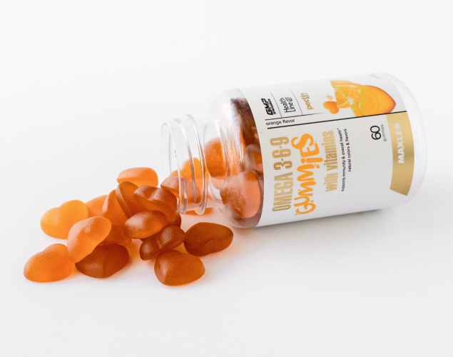 A photo of a laying Omega 3-6-9 bottle with a few gummies outside.